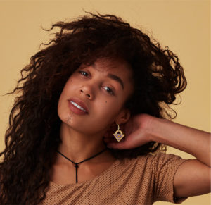 Fille brune avec des cheveux bouclés qui porte des boucles d'oreilles berbères